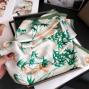 Close-up of bamboo leaf pattern silk scarf in luxury black gift box with hand model