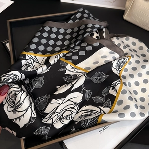 Detailed view of silk scarf with rose print, polka dots, and gold borders in a gift box