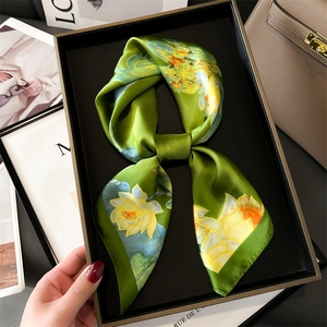 Detail of elegant green floral silk scarf with lotus print displayed on a luxury bag