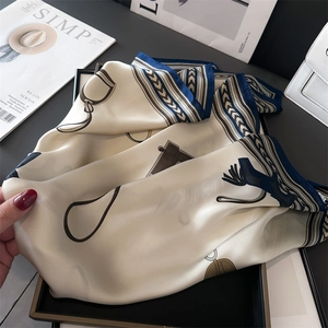 Detail view of a luxury satin scarf with classic horsebit and chain patterns on a tray