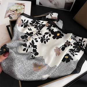 Vue détaillée d'un foulard en soie à fleurs avec bordure noire sur coffret cadeau