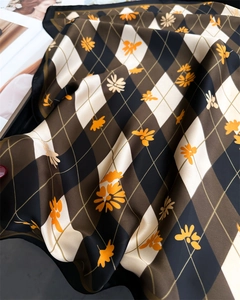Détail du foulard en soie avec motif en losange et fleurs orange avec bords roulés