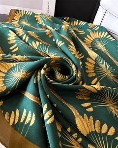 Gros plan d'un foulard en soie verte avec motifs de feuilles de palmier dorées