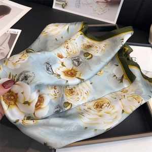 Dettaglio di sciarpa in seta floreale con logo Jardin Garden su tessuto azzurro