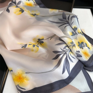Primo piano di un elegante foulard in seta con fiori gialli e motivi di foglie grigie