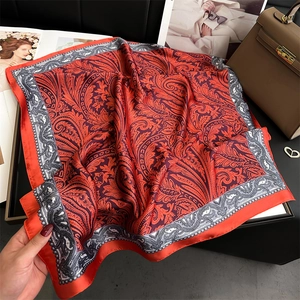 Dettaglio di un foulard in seta rossa con motivo paisley accanto a una borsa in cuoio