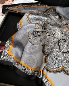 Close-up of paisley silk scarf in grey and black with vibrant orange border details