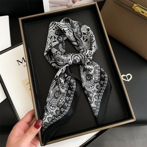 Close-up of black and white paisley silk scarf displayed in a luxury gold-rimmed gift box