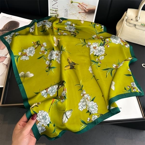 Detailed view of green floral silk scarf with butterflies on black leather surface