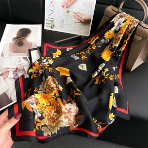 Elegant black silk floral scarf with yellow flowers and bold red border on leather surface