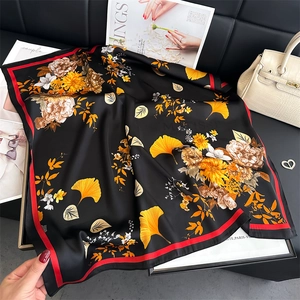 Detailed view of silk scarf with orange flowers and ginkgo leaves on black leather background