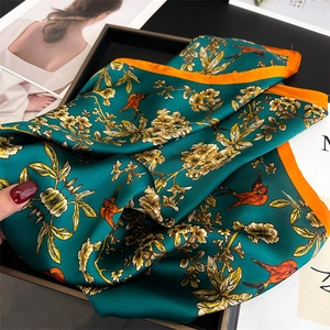 Detail of silk scarf with floral bird print and orange border on a black tray