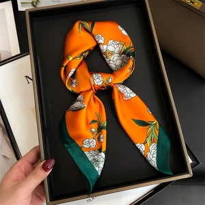 Detail of an orange silk twilly scarf with floral and butterfly patterns in a gift box