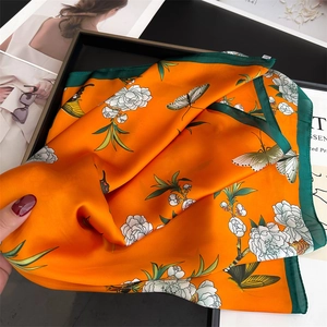Close-up of bright orange silk scarf featuring white flowers, butterflies, and green edges