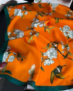 Close-up of elegant silk scarf with orange floral and butterfly patterns on a magazine