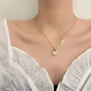 Goldene Titanstahl-Halskette mit Anhängern aus Schloss und Schlüssel auf asymmetrischer Kette