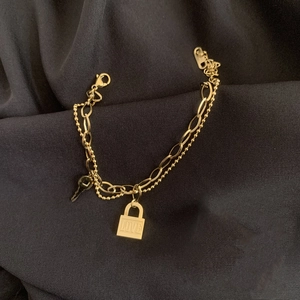 Detail eines goldenen zweilagigen Armbands mit Schloss- und Schlüsselanhängern