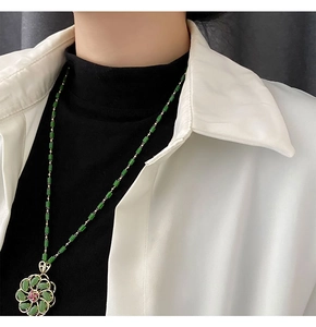 Detail of green floral pendant with red gemstone and beaded chain on a model