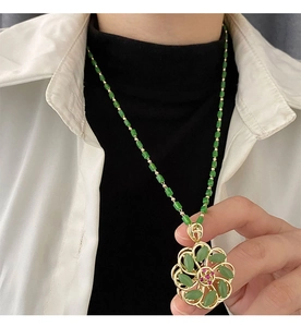 Close-up of green rotating lucky flower pendant with gold petals and jade beaded chain