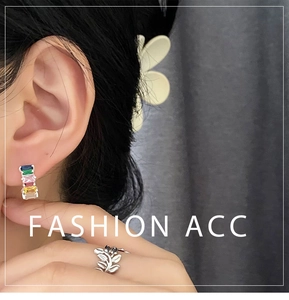 Close-up of colorful zircon rectangle earrings and silver leaf ring worn on a person