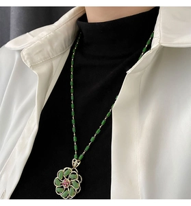Close-up of a green beaded necklace with a rotating gold floral pendant on a model