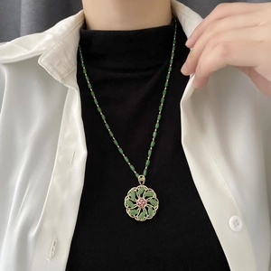 Rotating green floral pendant necklace with gold beads and red gemstone center