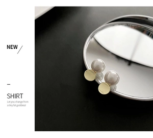 Elegant gold disc and faux pearl earrings reflected on a mirror over a black background