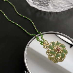 Rotating lucky flower necklace with green stones and golden beads on a mirror