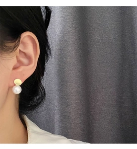 Detail of elegant pearl drop earring with gold disc on model with a soft gray background