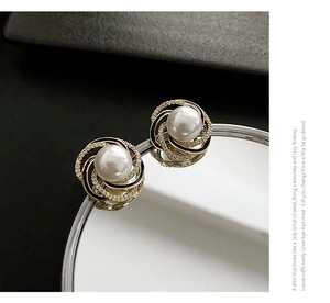 Macro shot of gold pearl stud earrings with zircon spiral design on mirror surface