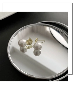 Detailed view of elegant round pearl earrings with gold posts on a reflective surface
