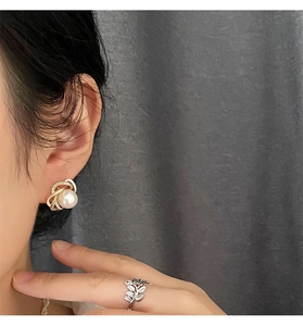 Detail of elegant pearl earrings and silver leaf-patterned ring on a female model