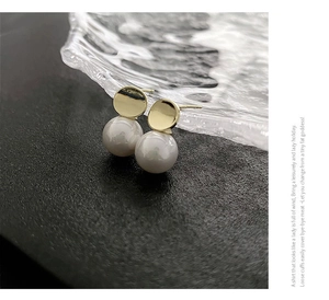 Macro shot of minimalist gold pearl stud earrings on a textured black surface