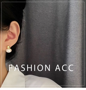 Close-up of gold metal ball and white pearl stud earring on model's earlobe