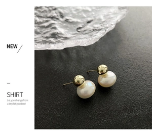 Detailed close-up of gold metal and white pearl stud earrings on a textured backdrop
