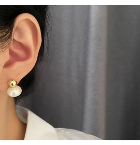 Macro side view of elegant golden metal stud earrings with dangling white round pearls