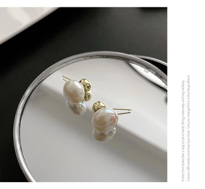 Close-up of elegant round white pearl earrings with gold-tone metal posts on a mirror