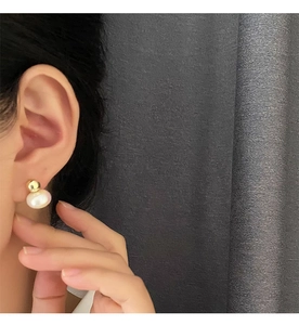 Close-up of elegant gold metal ball and white pearl stud earring on model's ear