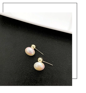 Macro detail of elegant baroque pearl earrings with golden studs on a black surface