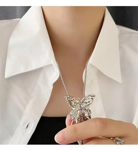 Dettaglio di una collana con ciondolo a farfalla argento con ali testurizzate su camicia bianca