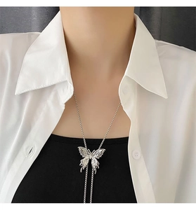 Dettaglio di un ciondolo a farfalla argento su una lunga catena di perline per maglia