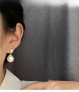 Close-up of elegant pearl drop earring with diamond-encrusted gold stud worn by model