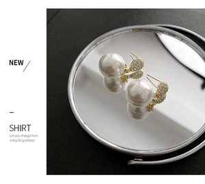 Macro detail of elegant pearl earrings with gold leaf-shaped diamond accents on mirror surface
