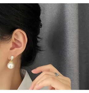 Detail of elegant pearl earring with micro-paved zircons worn by a female model