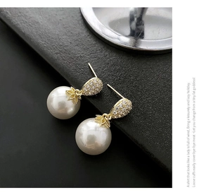 Detailed shot of pearl drop earrings with gold maple leaf accents and zircon studs
