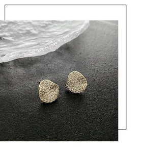 Detail of irregular gold earrings with micro-pave crystals on black textured backdrop