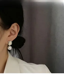 Close-up of geometric square metal earrings with a hanging white round faux pearl