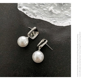 Macro detail of geometric pearl drop earrings with silver square metal clasp on dark stone