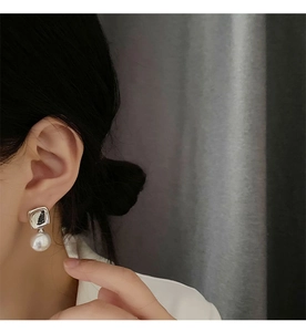 Close-up of geometric square silver earrings with white pearls worn by a model