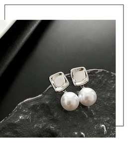 Close-up of geometric square silver earrings with large round pearls on textured glass